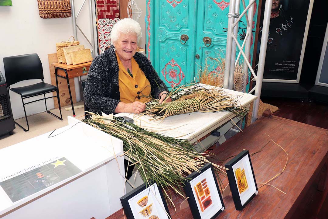 Elderly woman sitting at a desk with flax in front of her, used for weaving